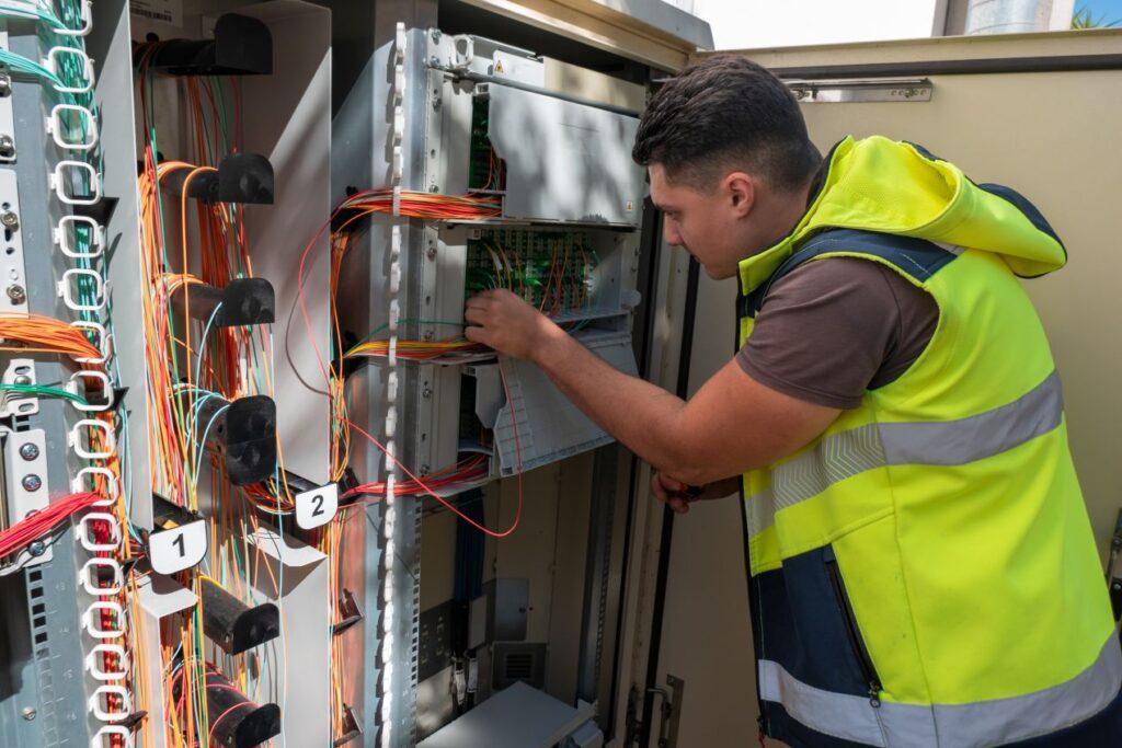Netzwerktechniker bei der Installation von MTP Steckverbindern in einem Outdoor-Verteilerschrank mit strukturierter Glasfaserverkabelung
